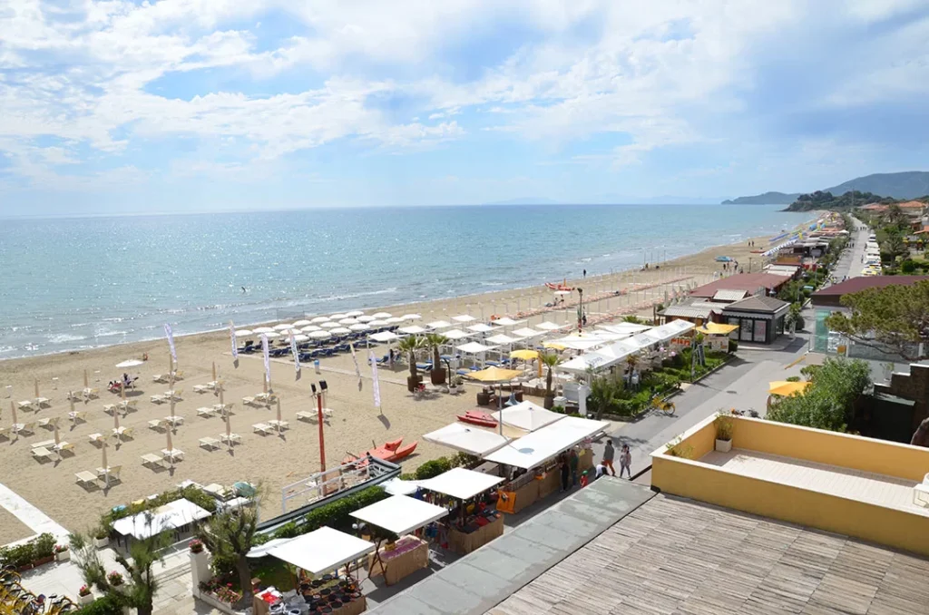 View of Castiglione della Pescaia from Hotel Miramare, showing the seaside town, marina, and surrounding hills under a clear blue sky on the Tuscan coast.