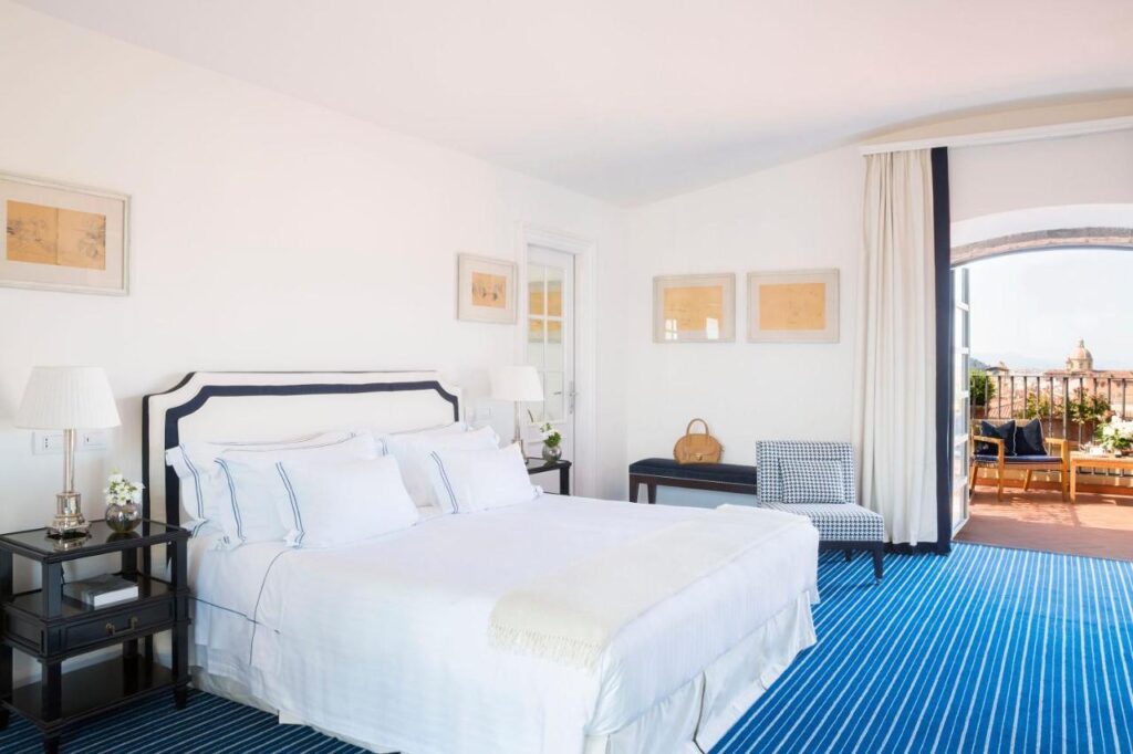 The 7 Best Luxury Hotels in Florence 18 Elegant bedroom at Hotel Lungarno in Florence with white bed, blue striped carpet, and private terrace access.