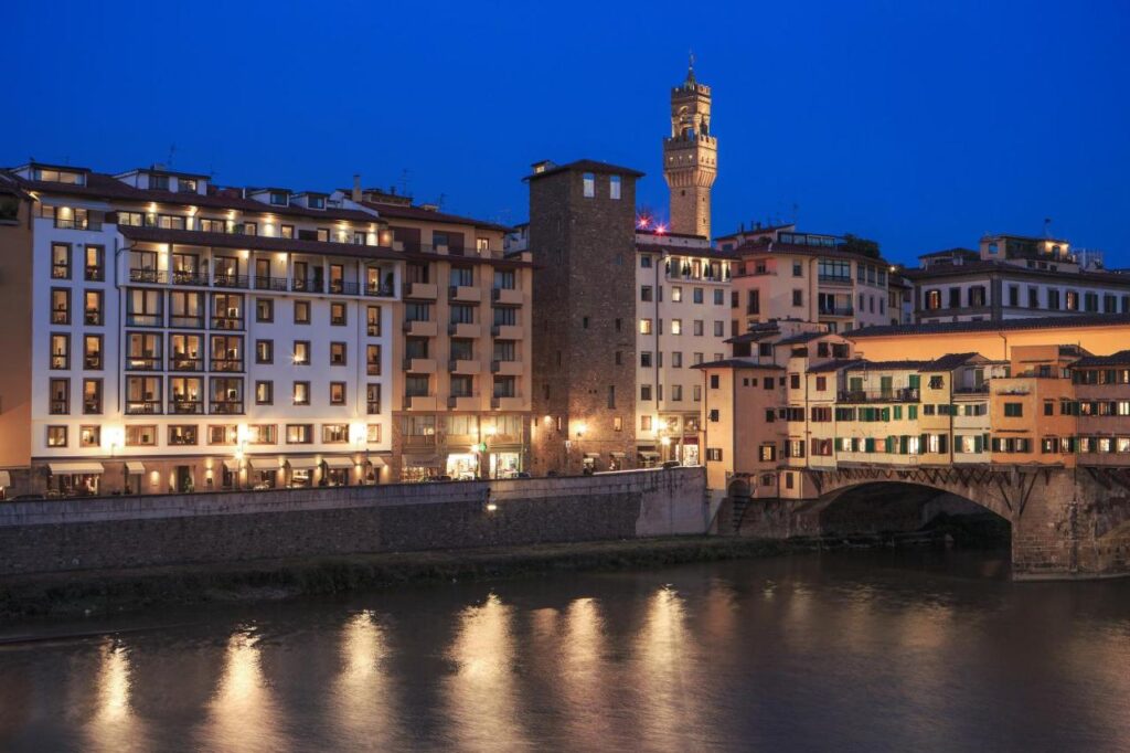 The 7 Best Luxury Hotels in Florence 30 Exterior view of Portrait Firenze hotel at night with illuminated facade overlooking the Arno River and Palazzo Vecchio in Florenc
