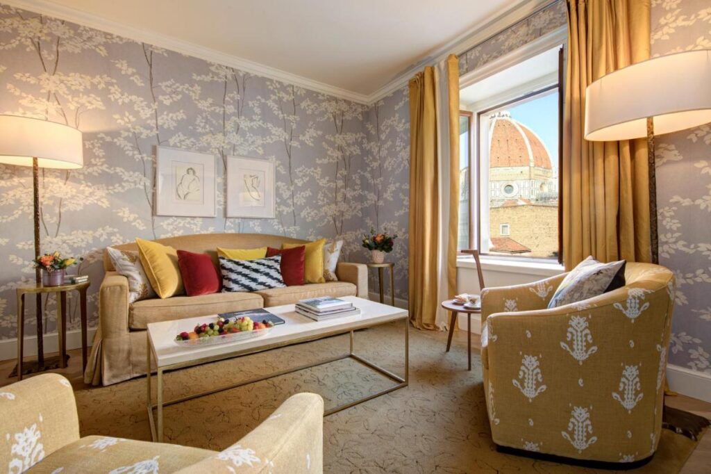 The 7 Best Luxury Hotels in Florence 9 Elegant hotel suite with soft yellow and beige tones, floral wallpaper, and a view of Florence’s Duomo from the window.