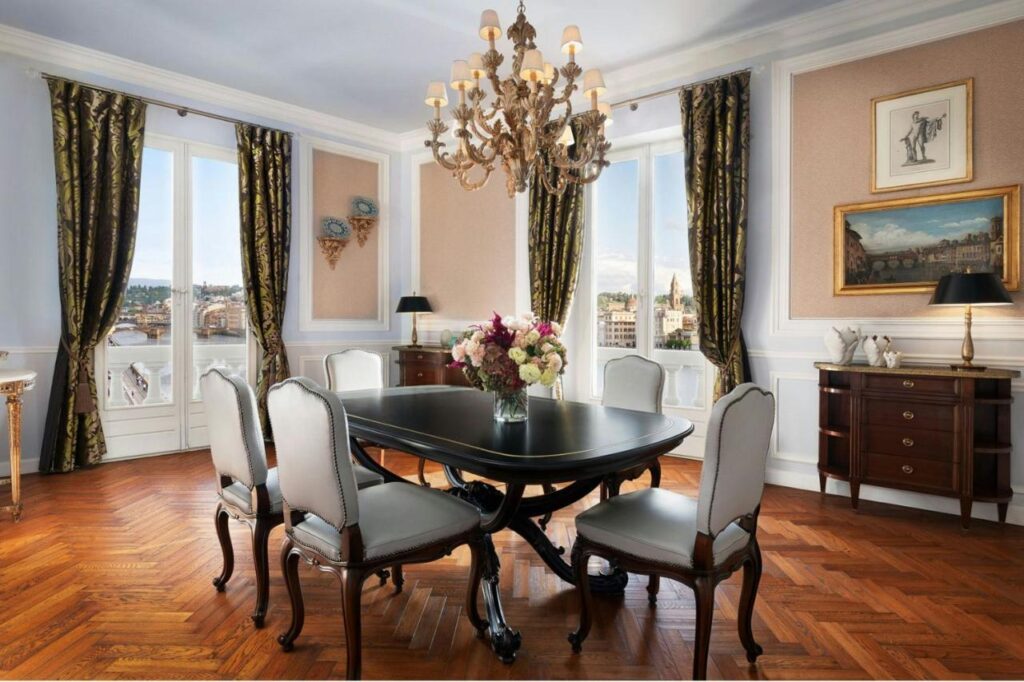 The 7 Best Luxury Hotels in Florence 5 Elegant dining room at The St. Regis Florence with a classic black table, white upholstered chairs, chandelier, and large windows overlooking the Arno River.
