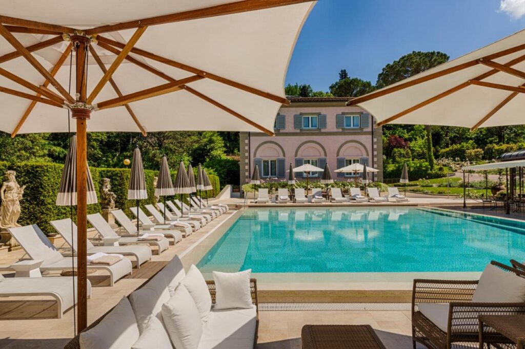 The 7 Best Luxury Hotels in Florence 24 Outdoor swimming pool at Villa Cora surrounded by sun loungers and parasols in a lush garden setting.