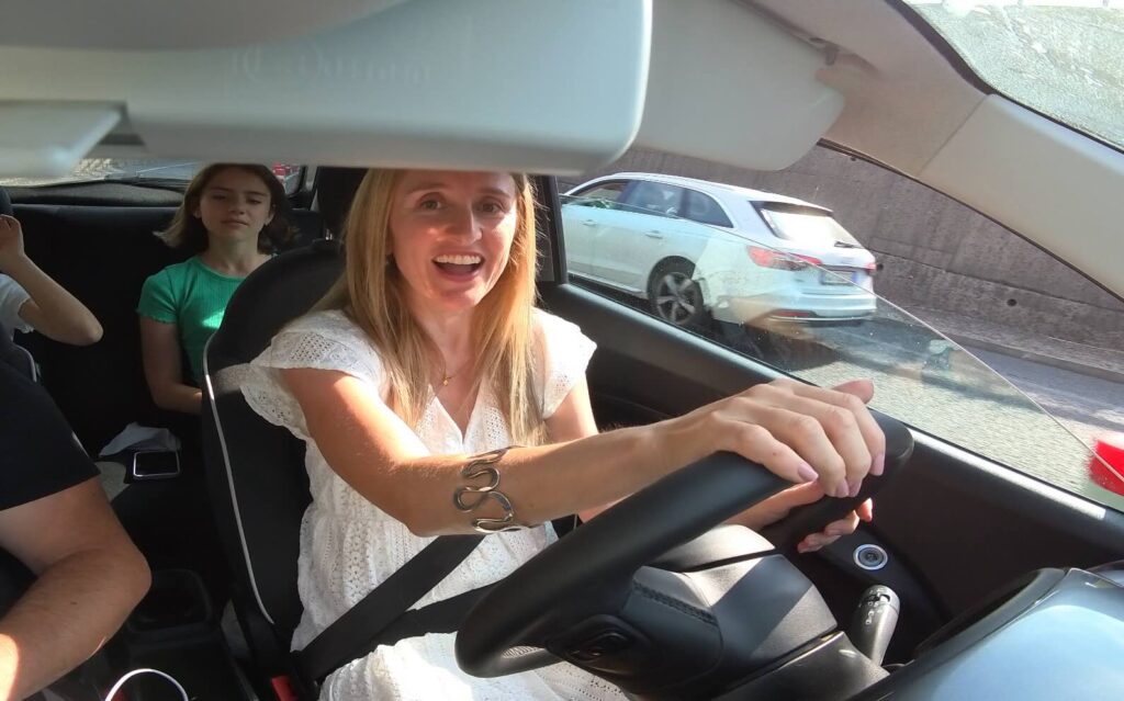 Woman smiling while driving an electric car in Tuscany, with two kids in the back seat. - Electric car rental in Tuscany 