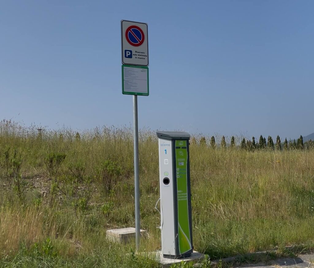 Electric vehicle charging station in a rural area near San Galgano Abbey, with a sign indicating reserved parking for EVs.