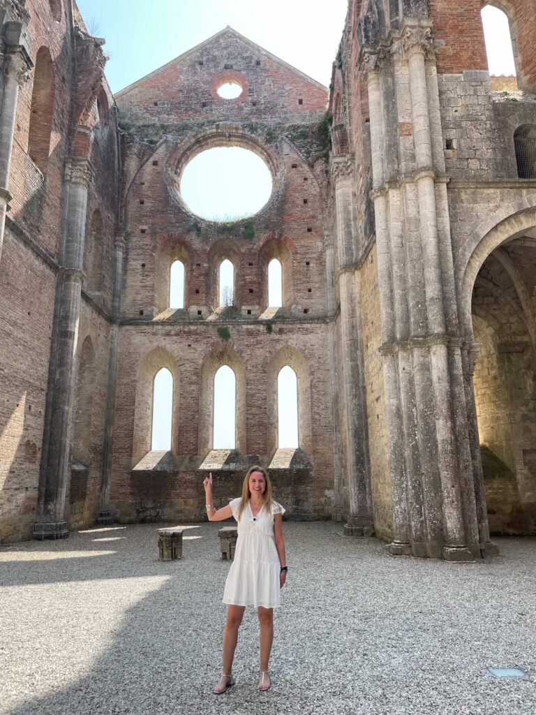Woman inside San Galgano Abbey in Tuscany pointing at the round window of the roofless church.