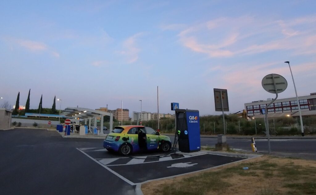 Electric car rented in Florence charging at a Q8 Electric station near Florence Airport, captured at sunset—perfect for travelers renting a car in Florence and exploring Tuscany sustainably.