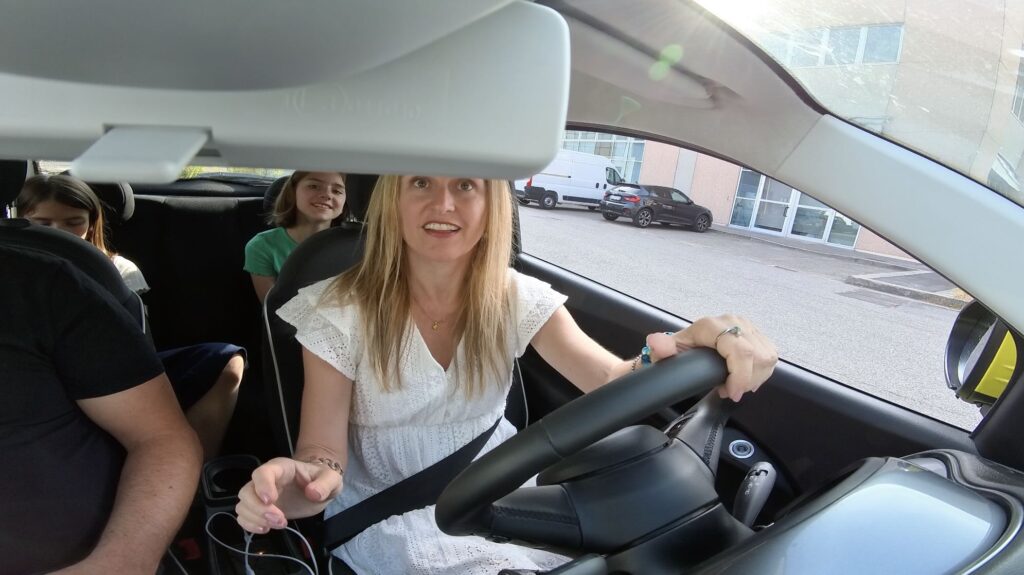 Woman driving a rented electric Fiat 500 in Florence with two children in the back seat; a compact, stylish Italian car ideal for city travel but with limited rear space and trunk capacity.