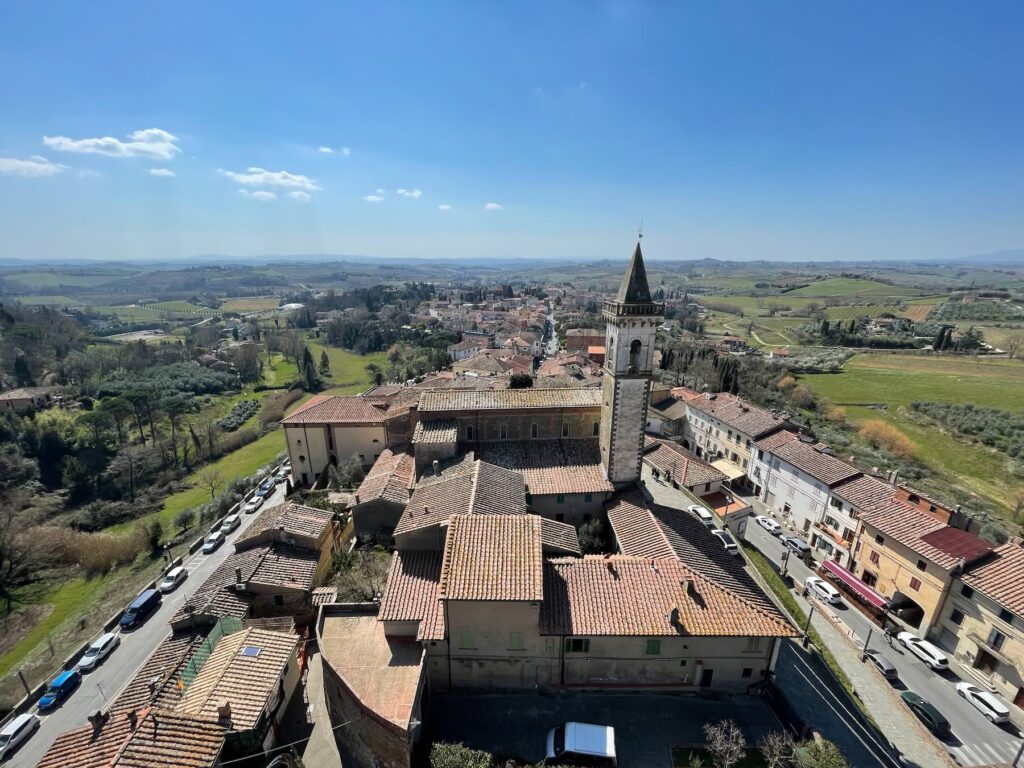 Aerial view of Vinci, Tuscany, with terracotta rooftops, a bell tower, and the surrounding countryside of rolling hills and olive trees. 