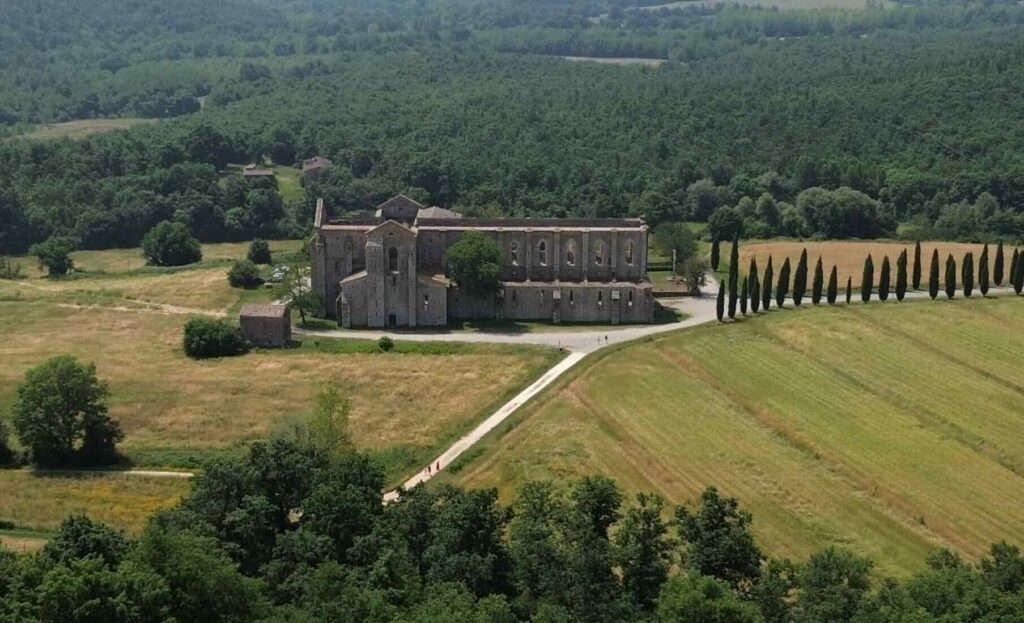 Aerial view of San Galgano Abbey in Tuscany, Italy, surrounded by fields and cypress trees.