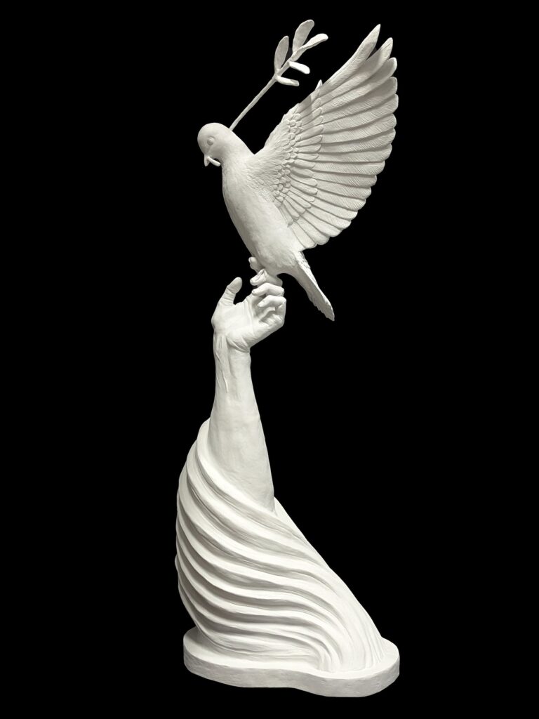 White sculpture by Cassandra Diaz depicting a hand releasing a dove carrying an olive branch, symbolizing peace, created for The Path to Paradise exhibition in Florence.