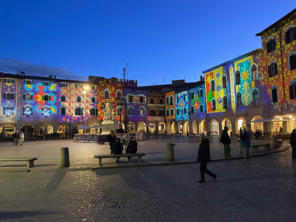 Evening view of Piazza Dante with vibrant Christmas light projections covering the façades of the square’s historic buildings in Grosseto.