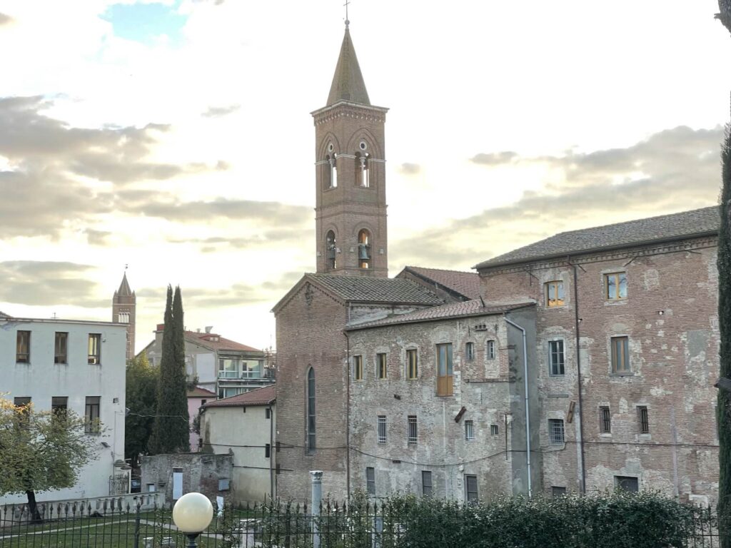 View of Grosseto’s historic bell tower and surrounding medieval buildings under a cloudy winter sky.