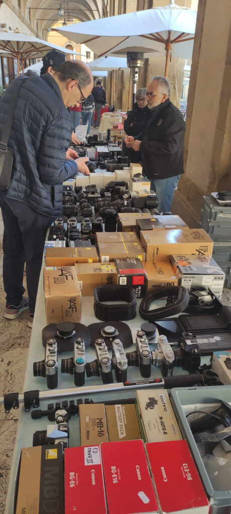 Visitors looking at tables filled with vintage cameras, lenses, boxes, and photography accessories at Foto Antiquaria in Arezzo.