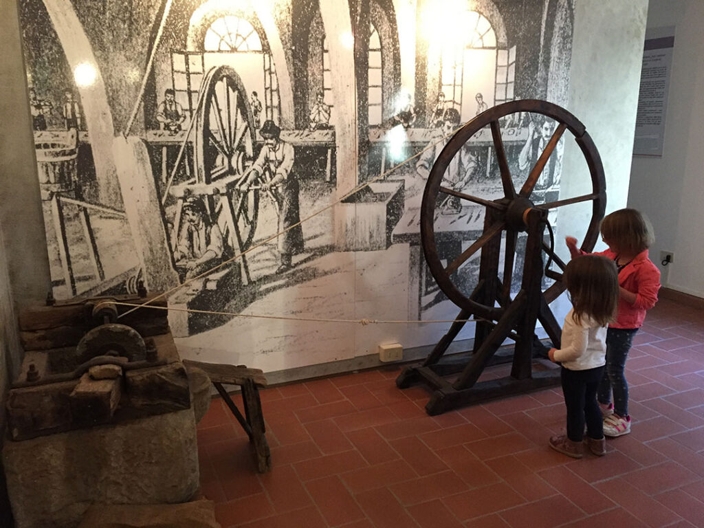 Children looking at a historic wheel mechanism inside the Museum of Cutting Tools in Scarperia, Tuscany.
