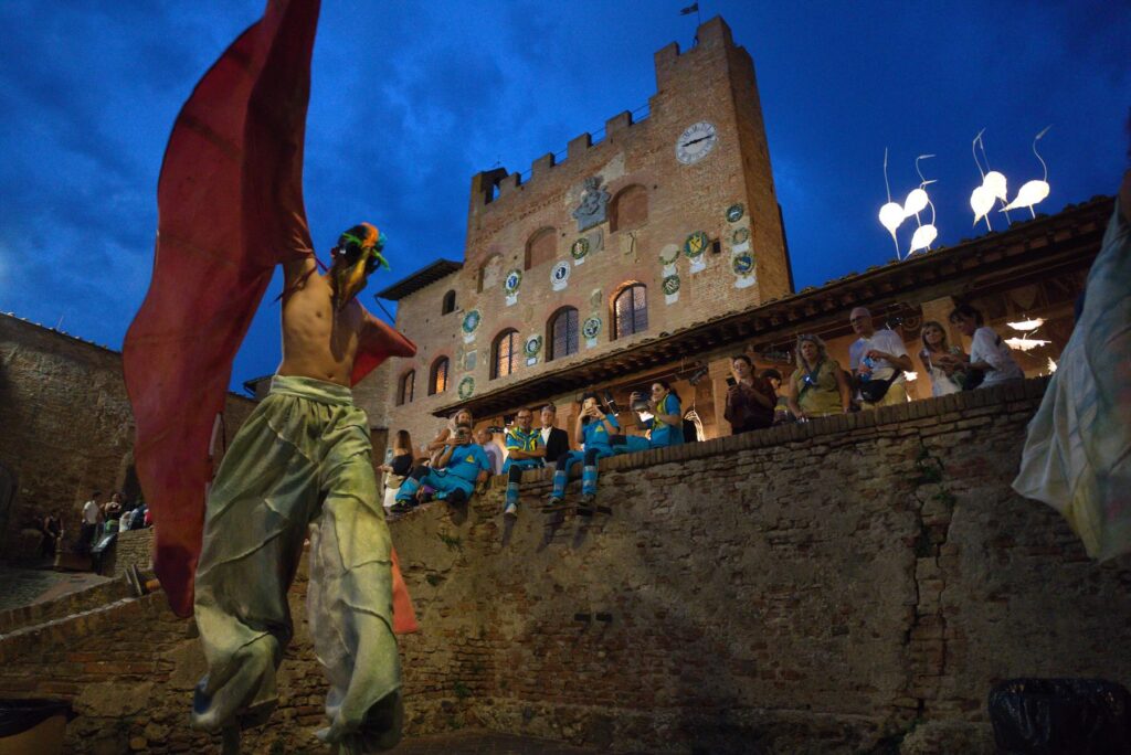 Street performer with large red wings in front of a medieval building during Mercantia in Certaldo, Tuscany.