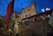 Mercantia in Certaldo 2026: Street Theater and Summer Magic in a Medieval Tuscan Town Street performer with large red wings in front of a medieval building during Mercantia in Certaldo, Tuscany.