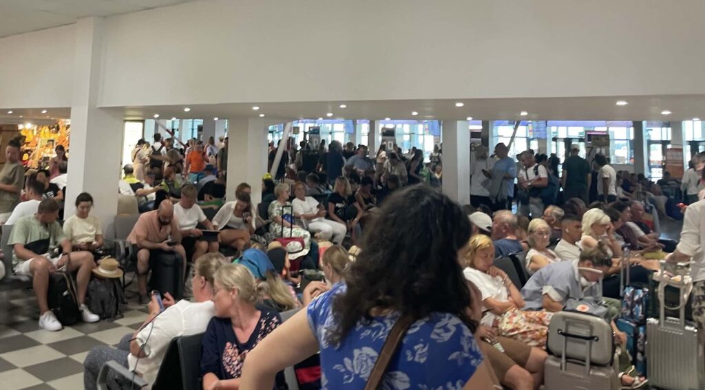 Flight delays in Tuscany: current EU rules and what is changing for travelers 2 Crowded waiting area at Pisa Airport with passengers seated and standing with luggage during a day of flight and boarding delays.